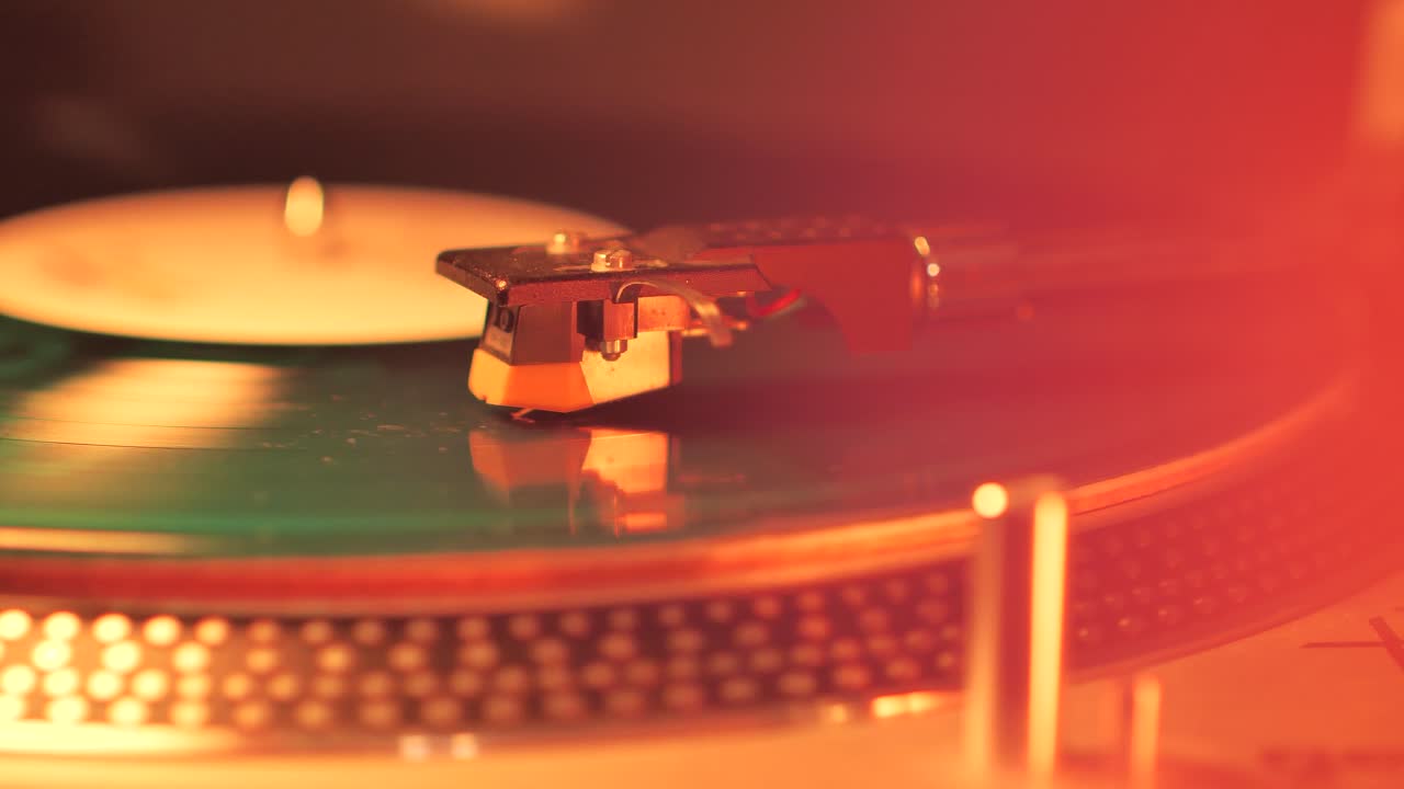 A Rotating Vinyl Record on a Turntable in the Light of a Warm Orange-Red Lamp. A dusty green colour LP Vinyl Disc Record Close-up Playing Music. Type C.
