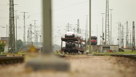 Car-transport-train-loaded-with-new-vehicles-at-a-rail-yard,-foreground-focus-on-tracks