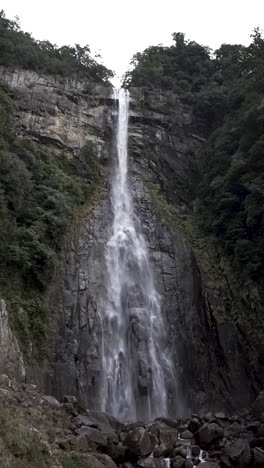breathtaking view of nachi falls flowing over rugged cliffs surrounded by greenery. vertical video, slow motion