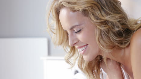 mujer rubia acostada en la cama usando una computadora portátil