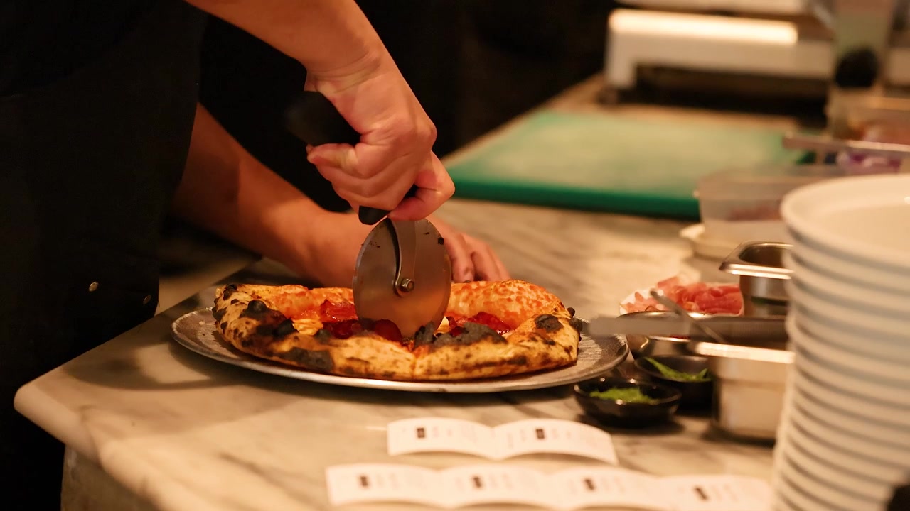Chef che taglia una pizza al salame piccante appena sfornata nella cucina di un ristorante.