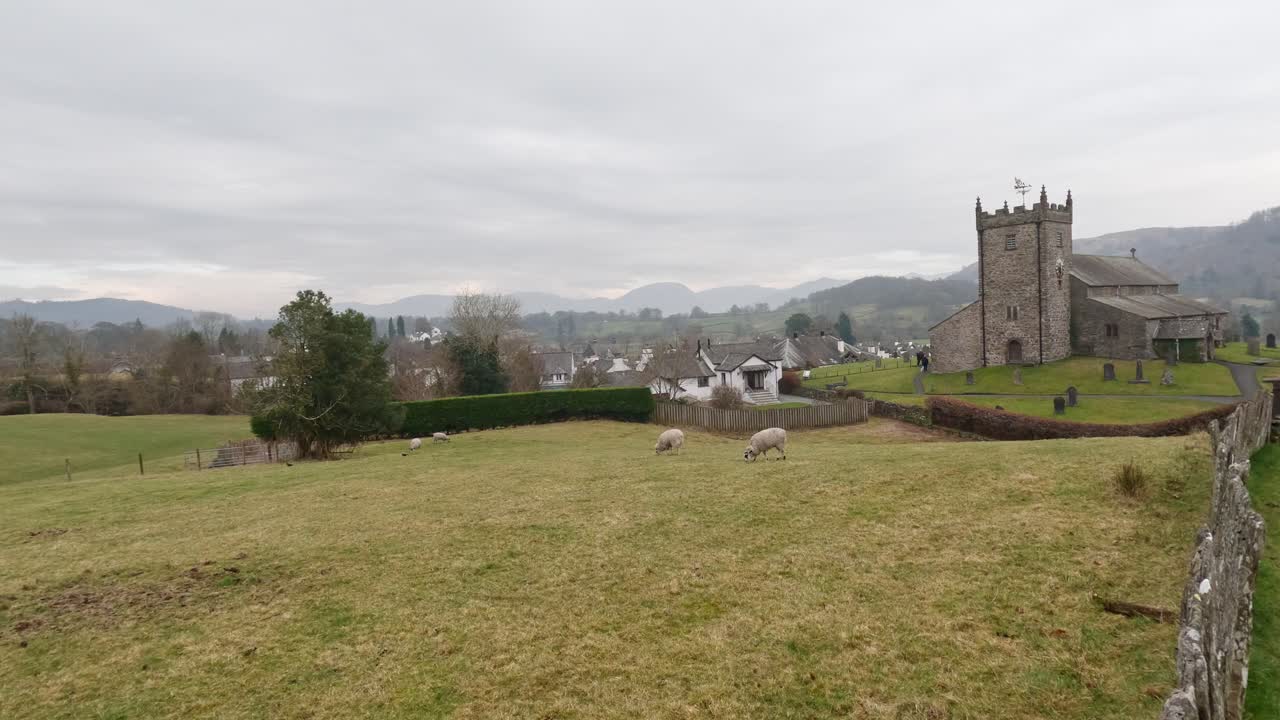 St. Michael og Alle Engle Kirke i Hawkshead, viser marker og græssende får, Cumbria, Storbritannien