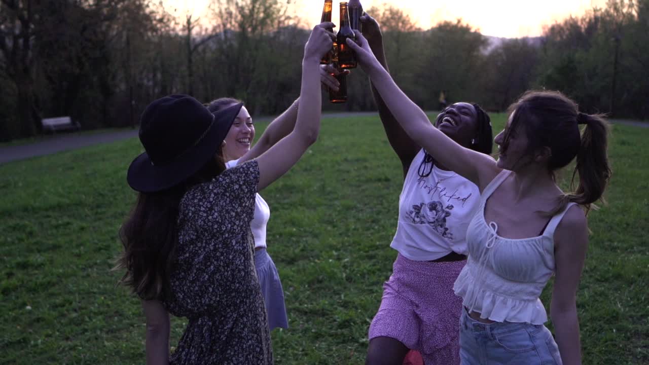 compañía de amigas multirraciales haciendo sonar botellas en el parque al atardecer