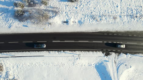 Varios-Autos-Conducen-Uno-Tras-Otro-Mientras-Otros-Vehículos-Conducen-En-La-Otra-Dirección-En-Una-Carretera-Asfaltada-Negra-Despejada-De-Nieve-Blanca