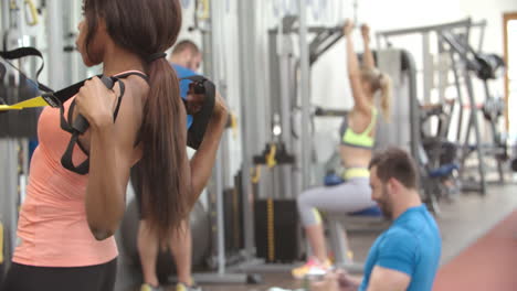 mujer joven entrenando con correas de resistencia en un gimnasio ocupado