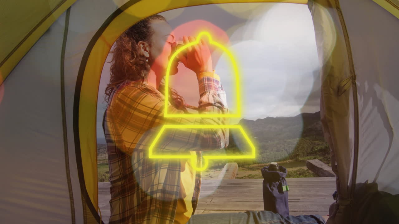 woman sipping mug inside yellow tent on wooden deck, showcasing neon bell icon overlay for travel