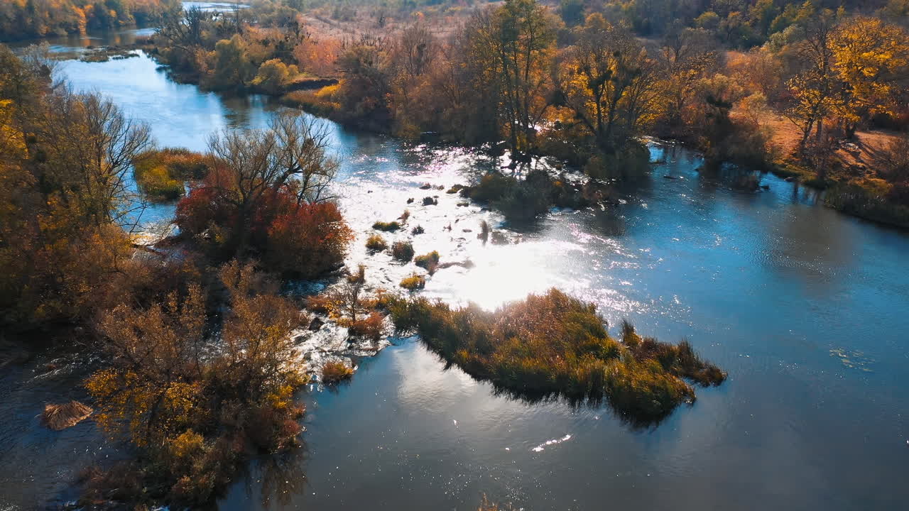 Beautiful nature in sun flare. Autumn scenery. Blue lake among yellow and orange trees. Amazing wild nature. Aerial view.