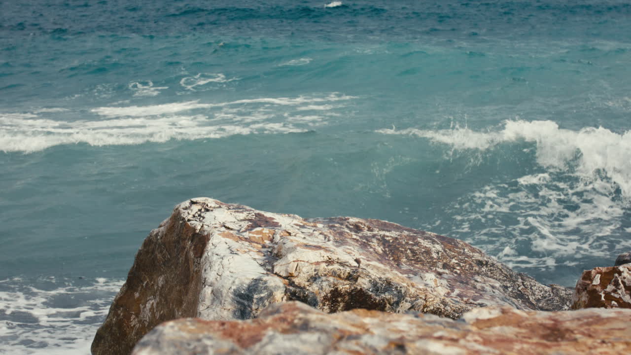 Slow motion shot of a crashing wave striking golden coastal cliffs. Bright blue water and sharp contrast in textures create a vivid natural impact