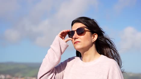 woman wearing sunglasses being dazzled by the sun in a windy day, handheld shot