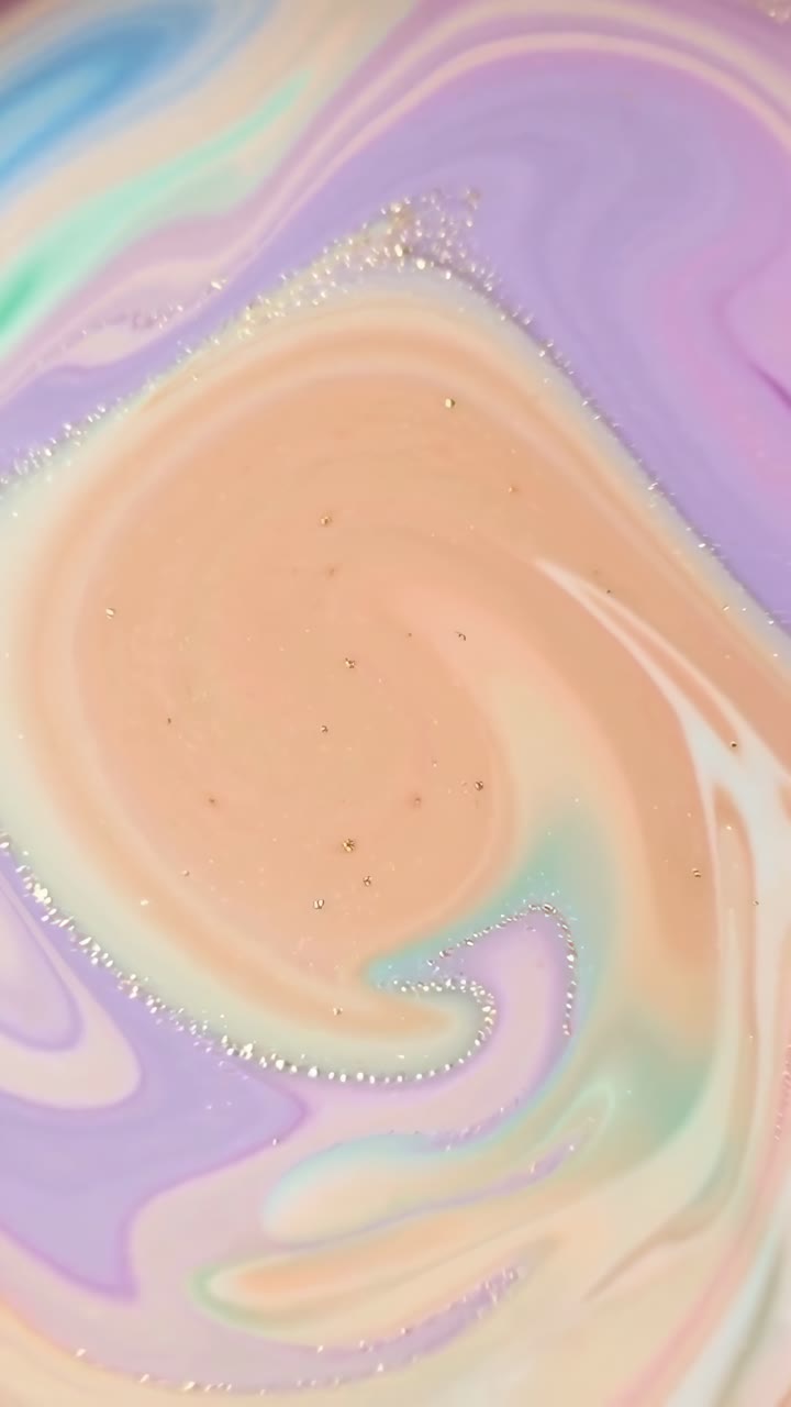 Video cenital de colores pastel arremolinados con purpurina, creando un efecto onírico y abstracto
