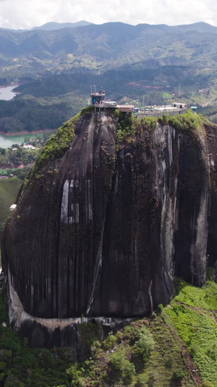 Aerial view of El Penon de Guatape, a massive rock dominating the landscape with a staircase built into its side leading to a viewing platform. Vertical Video