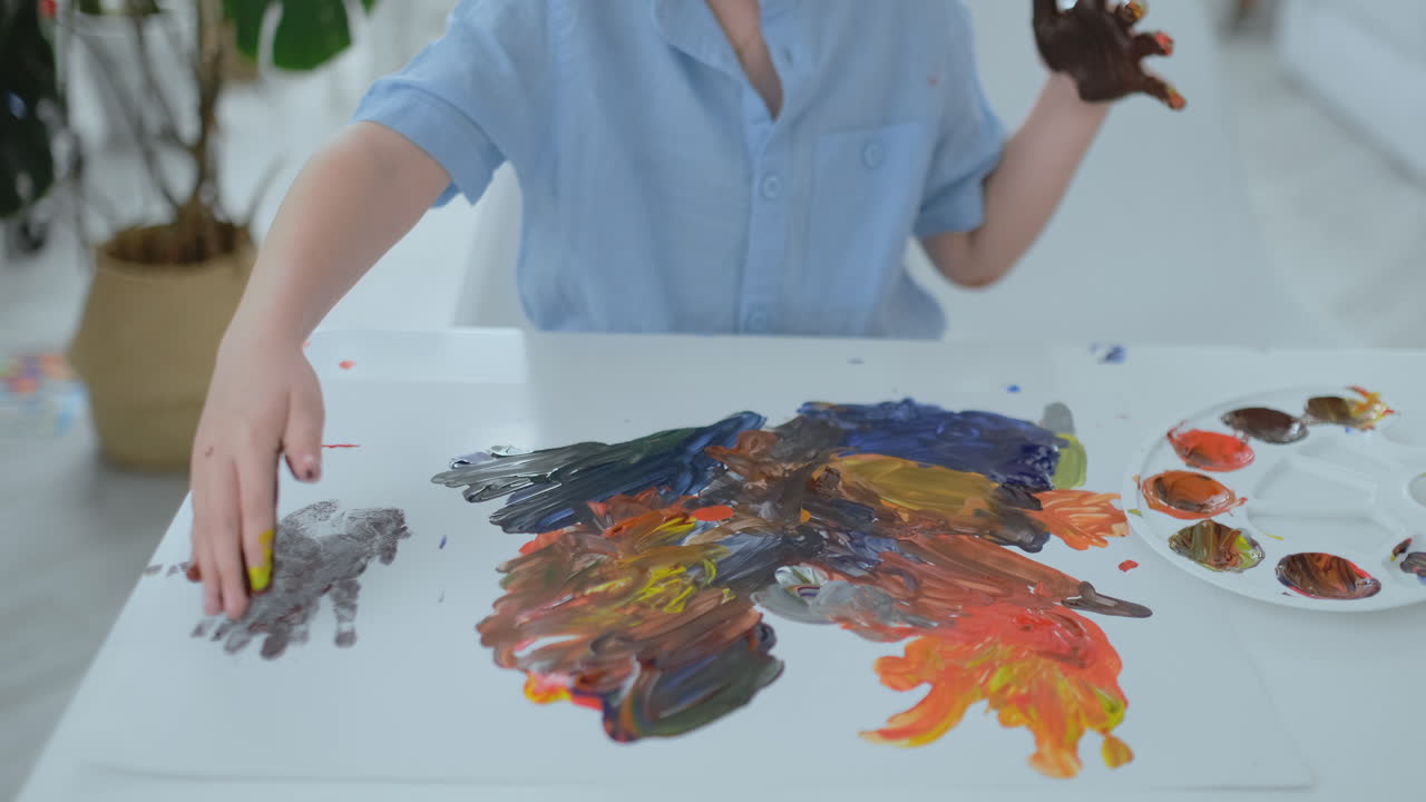 소년은 지저분한 도움으로 종이에 손발자국을 남 ⁇ 니다. pomuschiyu 페인트로 손가락을 그립니다. 어린이의 창의적 능력의 발달