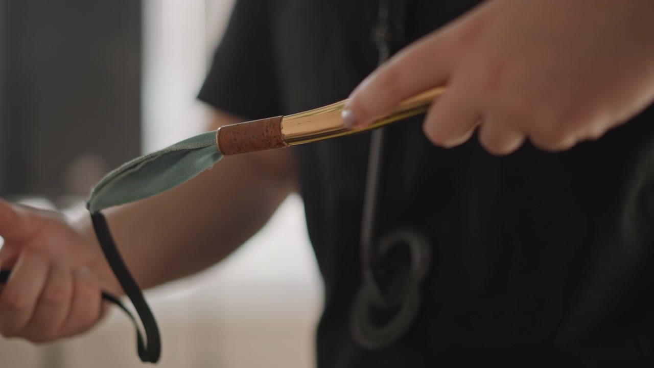 Young musician prepping saxophone with cloth and strap closeup, hands carefully cleaning mouthpiece and polishing brass, classroom light, instructor guidance visible in background, focused rehearsal