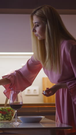 pretty young woman in pink dress pours poisonous powder into glass with red wine of partner offender before romantic dinner in kitchen slow motion