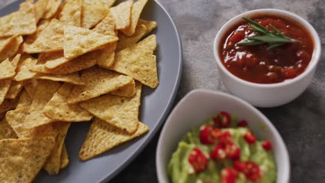 close up of nachos in a plate and sauces on black surface