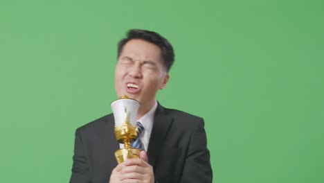 close up of asian business man in a suit and tie with a gold medal singing on a gold trophy celebrating winning as the first winner on green screen background in the studio