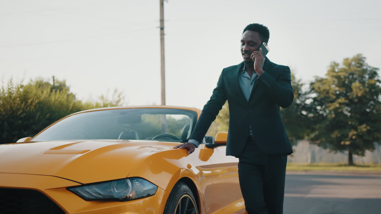 un hombre de negocios hablando por teléfono al lado de un descapotable amarillo.