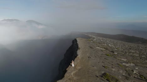 blond angelic woman in white dress walks along ijen volcano crater edge