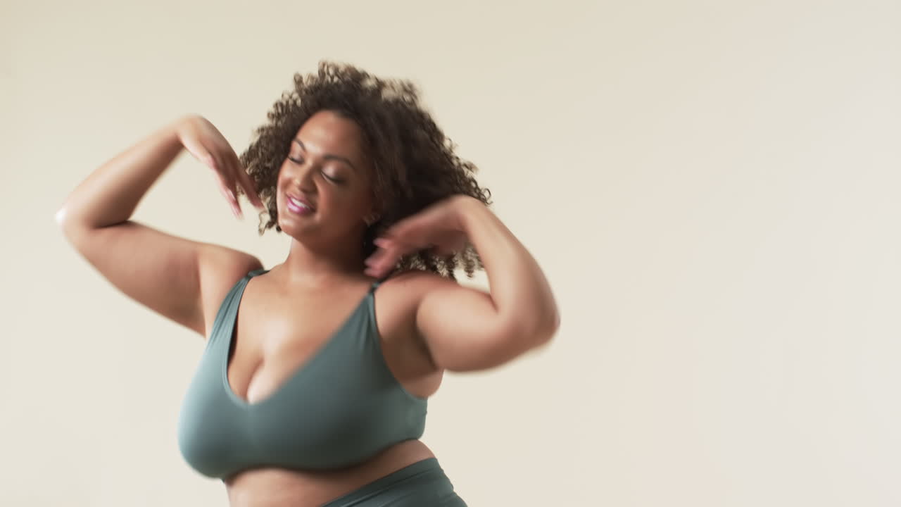 A plus size woman with curly hair wearing green sports bra is dancing joyfully