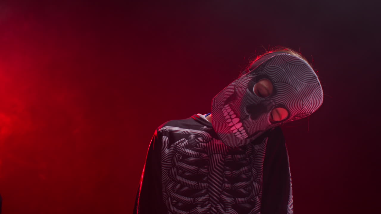 fotografía de estudio de un niño vestido con un disfraz de esqueleto con los ojos cerrados haciendo trucos o tratamientos en halloween con iluminación de fondo de humo rojo