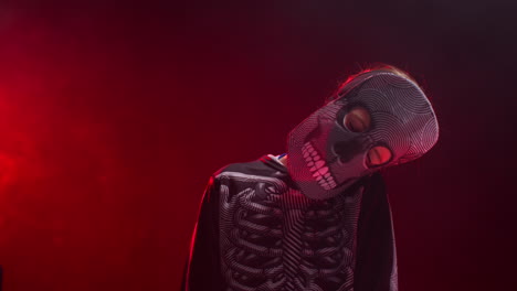 studio shot of child dressed up in skeleton costume with closed eyes trick or treating at halloween with red smoke background lighting