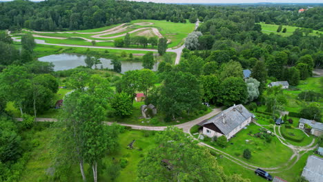 revealing drone view of lush green homestead with pond and offroad track visible