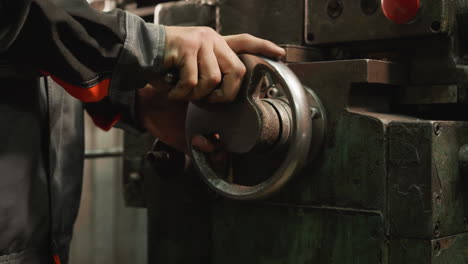 worker's hand on a lathe wheel with industrial machinery in a metalworking shop