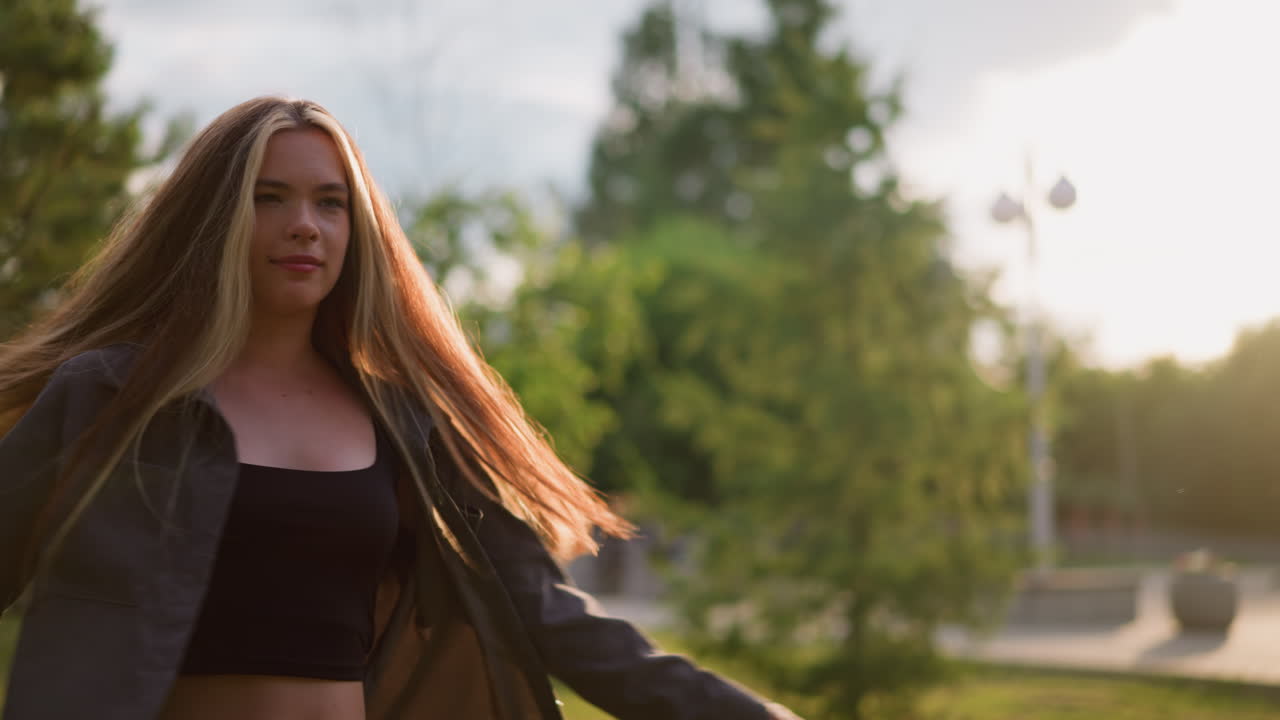 леди с радостью поворачивает по часовой стрелке в травяном поле под ярким солнечным светом, создавая сияющую атмосферу, на заднем плане зеленые цвета, деревья и здания