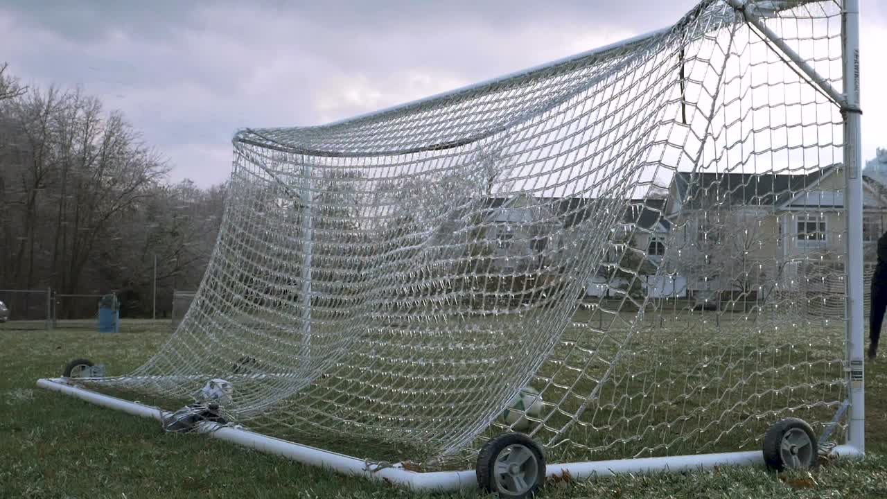 cámara lenta: una pelota de fútbol es pateada y golpea una red helada de un gol de fútbol que explota hielo destrozado en el aire con una camioneta en el fondo