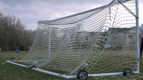 SLOW-MOTION:-A-soccer-ball-is-kicked-and-slams-an-icy-net-of-a-soccer-goal-exploding-shattered-ice-into-the-air-with-a-van-in-the-background