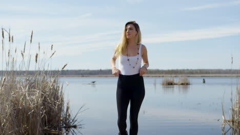 confident trendy young woman walks towards the camera, lake in the background