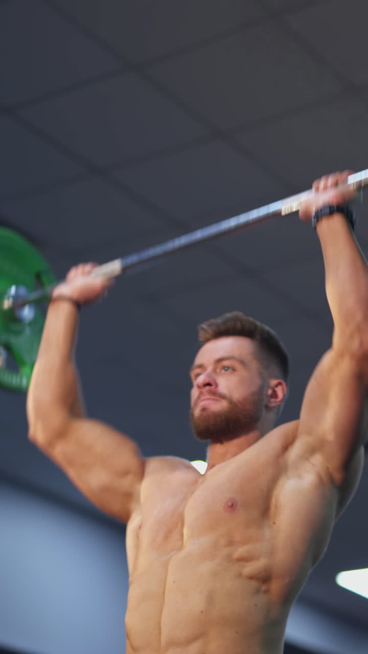 Bodybuilder raising barbell over his head. Young shirtless sportsman exercises his maintain muscle in gym. The active man lifting a barbell. Handsome athlete doing weight lifting. Vertical video