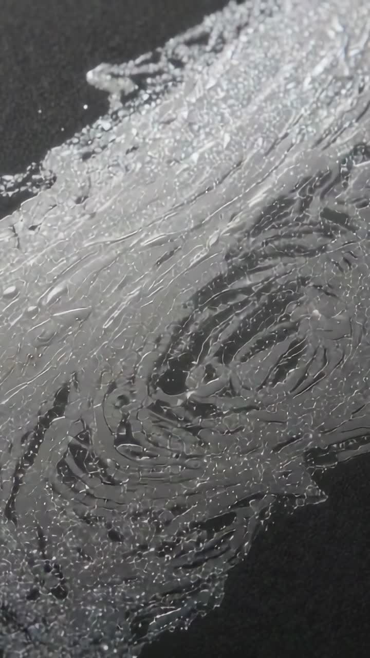 Vertical video: Shifting camera revealing viscous smear on dark tabletop to reveal swirl texture