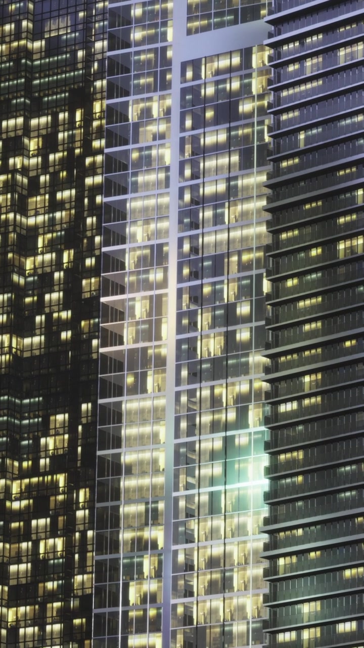Luzes de edifícios brilham intensamente em uma cidade à noite com estruturas altas por perto.