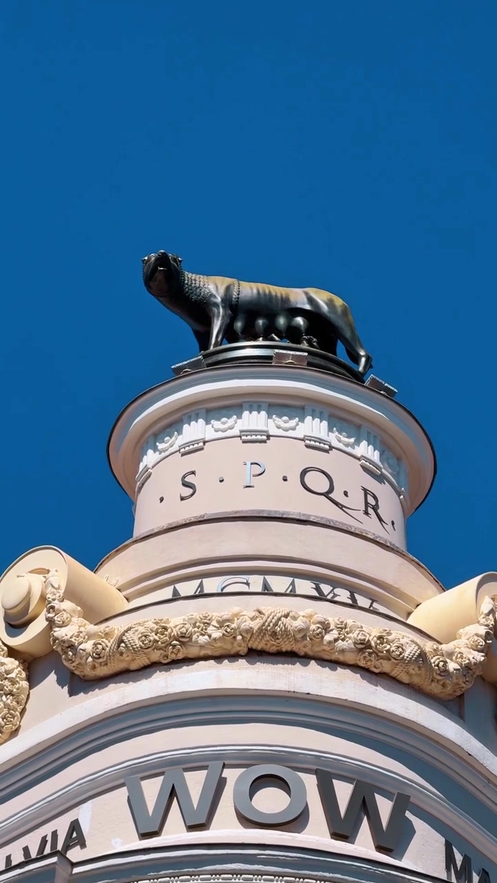 Madrid, Spagna, 8 agosto 2025: Dettaglio architettonico della cima di un edificio in Gran Via a Madrid. Primo piano della facciata dell'edificio con la statua della Lupa Capitolina e l'iscrizione SPQR contro un cielo azzurro limpido a Madrid.