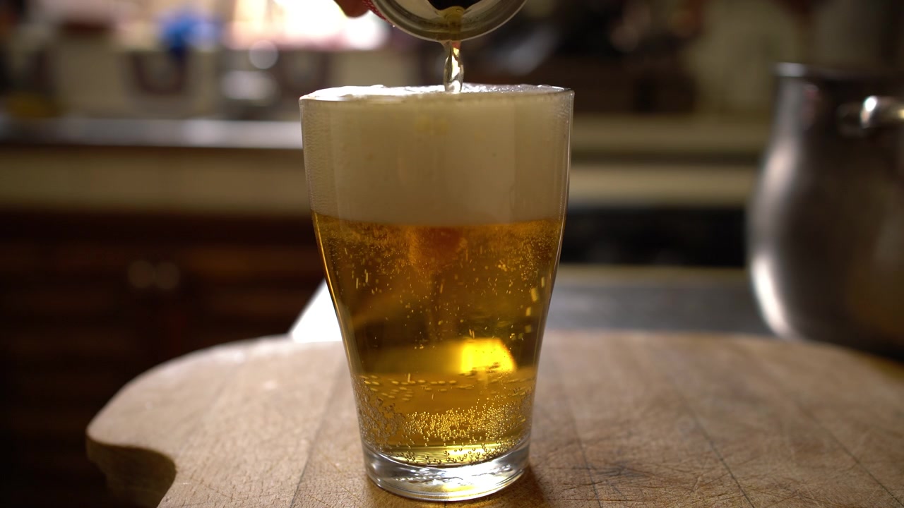 Un bicchiere su un tavolo di legno si riempie di birra versata da una lattina mentre la schiuma si deposita in superficie, Inquadratura statica