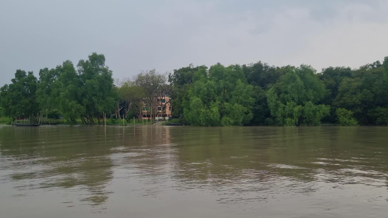 Boat view along the Pasur River near Mongla in the Sundarbans, Bangladesh, showing tidal waters, dense tropical vegetation, and a cloudy monsoon sky over the tranquil river delta