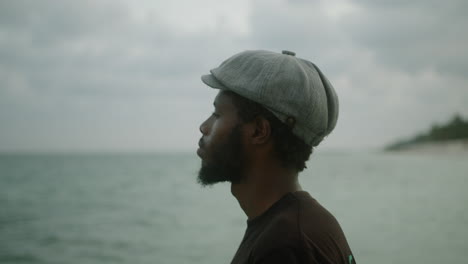 close-up of a handsome young black bearded man in a beret looking out over the ocean introspectively