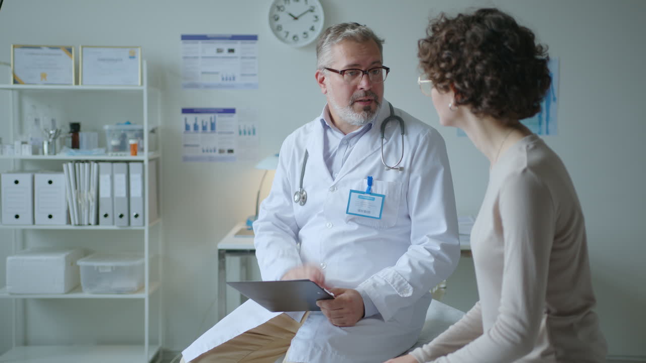 Doctor Talking to Patient Sitting on Examination Table in Medical Office