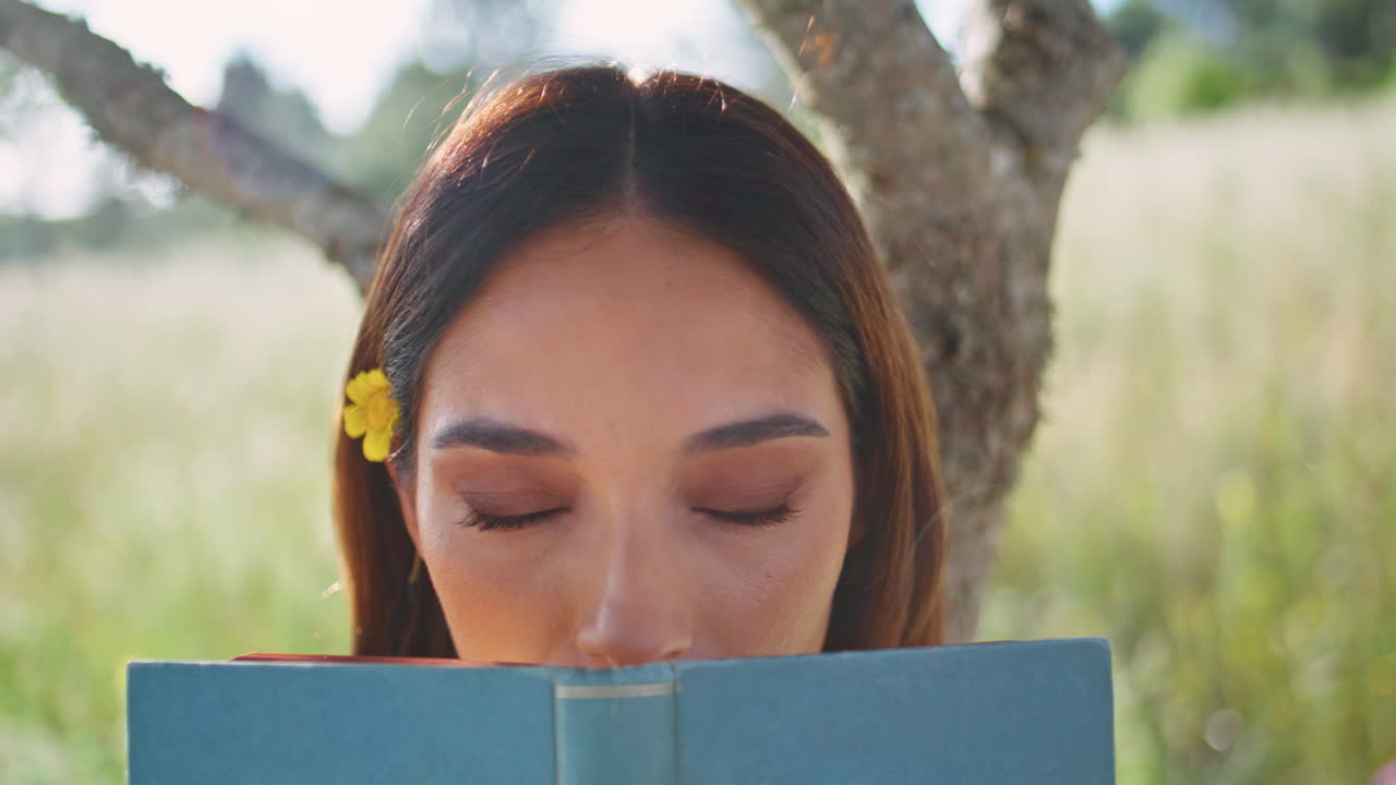 Playful model holding book hiding face at field nature portrait. Lady posing