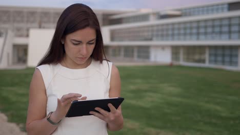 Focused-young-redhead-girl-using-modern-tablet-outdoor.