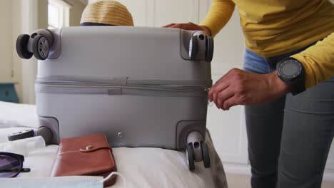 Hands-of-biracial-woman-zipping-suitcase-ad-taking-passport-with-face-mask