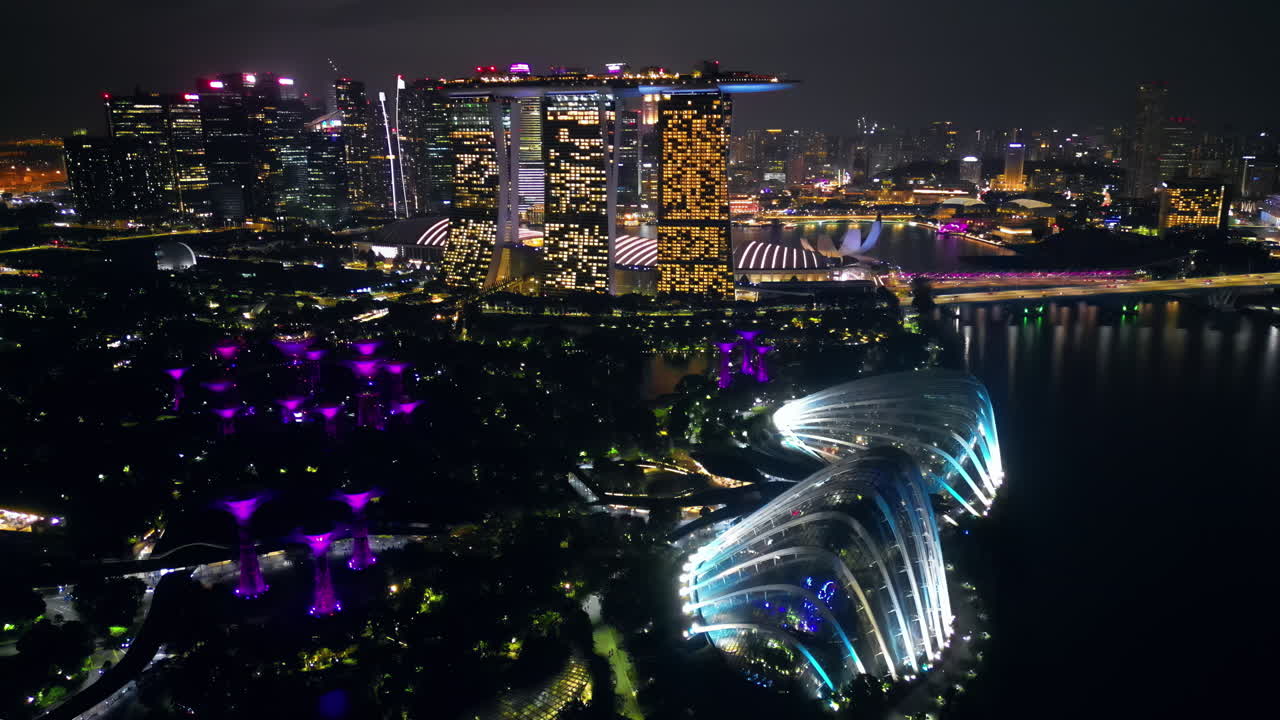 Vista aerea con drone di Marina Bay a Singapore di notte, che mostra il Marina Bay Sands, la ruota panoramica Singapore Flyer e lo skyline illuminato del lungomare