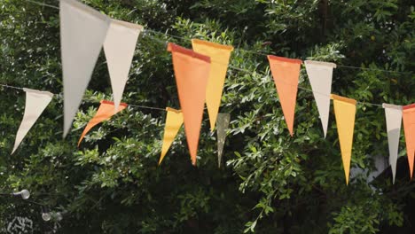 white, yellow and orange triangle flags hang on white rope in garden view. garland flags are blowing .concept : fun party.