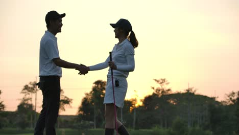 golfing couple handshake on the sunset background. two asian golf player male and female shaking hands in glow of the sunset. slow motion.
