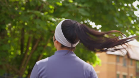 rear view of young woman exercising running along urban street wearing wireless earbuds 2