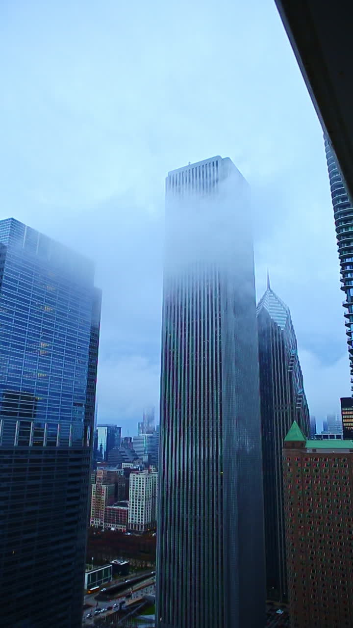 Nuvens se movem ao redor de arranha-céus em uma cidade movimentada durante um dia nublado, com um toque de neblina criando uma atmosfera sobre o horizonte da cidade.
