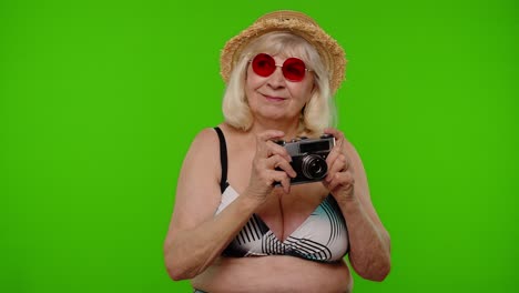 senior woman wearing a bikini and hat taking a picture with a camera on green screen background