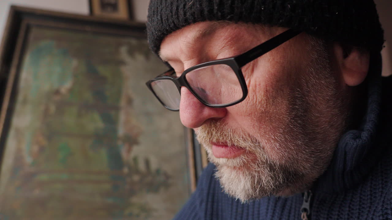 Middle aged man in glasses ponders his personal thoughts while writing in a journal. The low lighting creates a moody, atmospheric setting perfect for themes of reflection and solitude