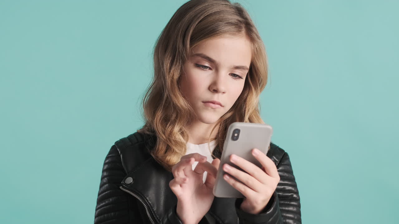 가죽 재을 입은 십대 백인 소녀가 스마트폰을 사용하고 있습니다.